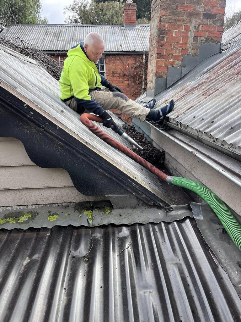 A photo of john sitting on a customers roof using his gutter vacuum to clean away leaves from the gutters in a customers home in Bendigo, Victoria